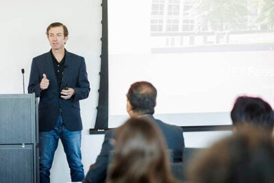 A man in a sport coat standing next to a podium speaks to people who are sitting in front of him.